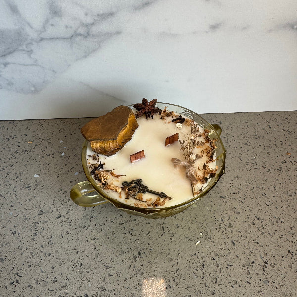 Decorative candle with herbs on a gray surface next to a marble wall
