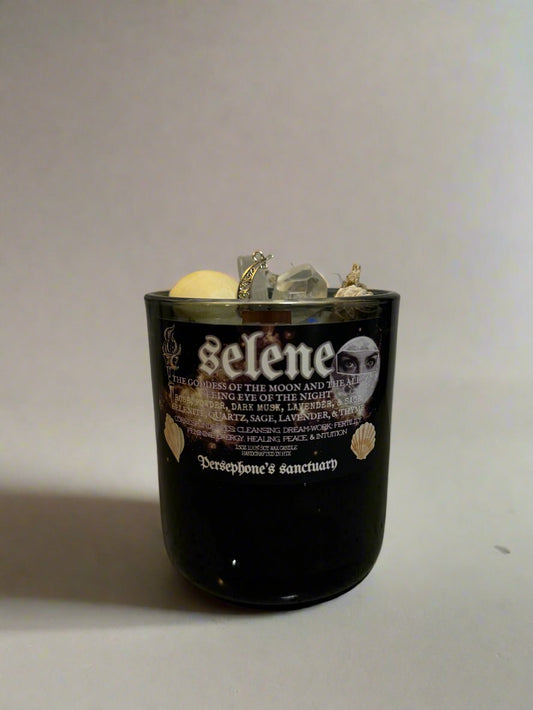 A black Selene candle in a tin container with a label featuring the name 'Selene' and a graphic of a crescent moon, along with text describing the candle as a 'Spiritual Candle' with elements such as selenite and quartz.