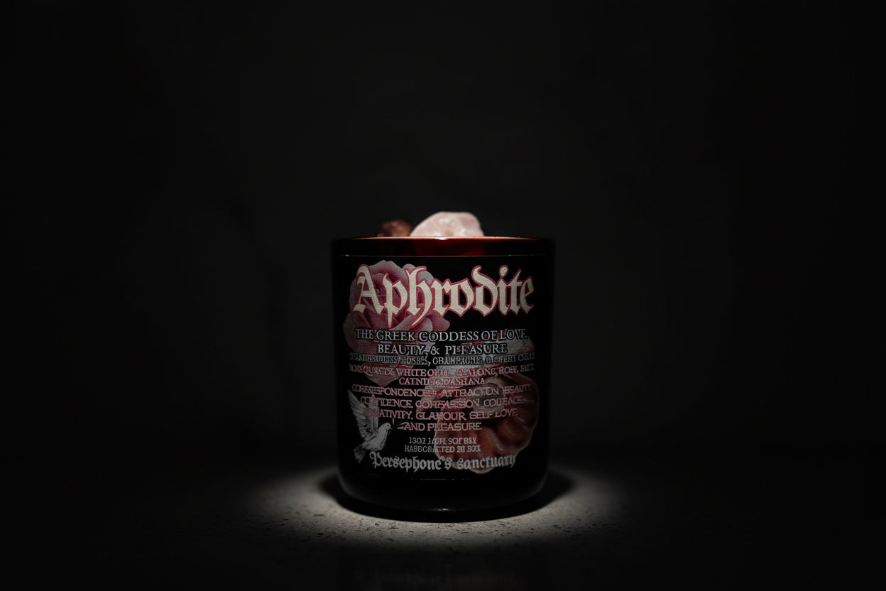 A red jar candle labeled 'Aphrodite' with rose quartz crystals on top, set on a marble surface.