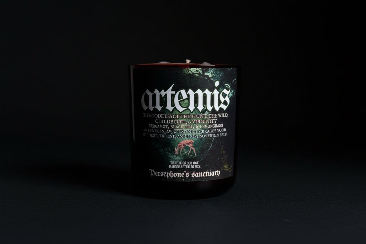 A black candle with a label featuring the name 'artemis' and an illustration of a deer. The candle is branded as 'Persephone's Sanctuary' and has various stones and plants depicted around it.