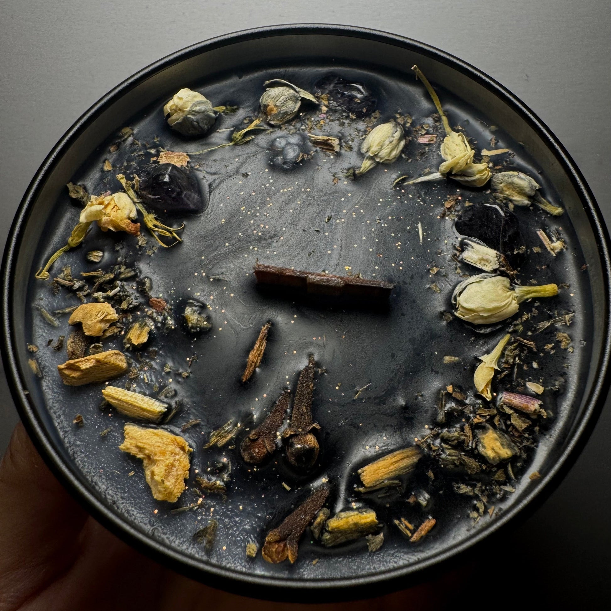 Black candle with dried herbs and flowers 